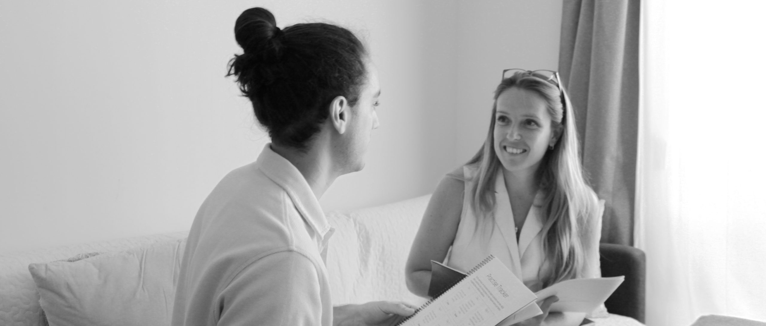 a man and a woman sitting on a couch with workbooks in their hands, facing each other